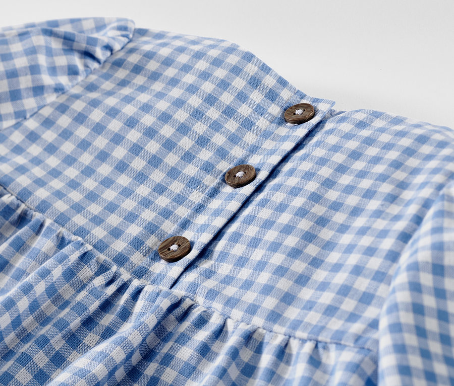 Detail detských tkaných šiat s modro-bielou kockou a gombíkmi.