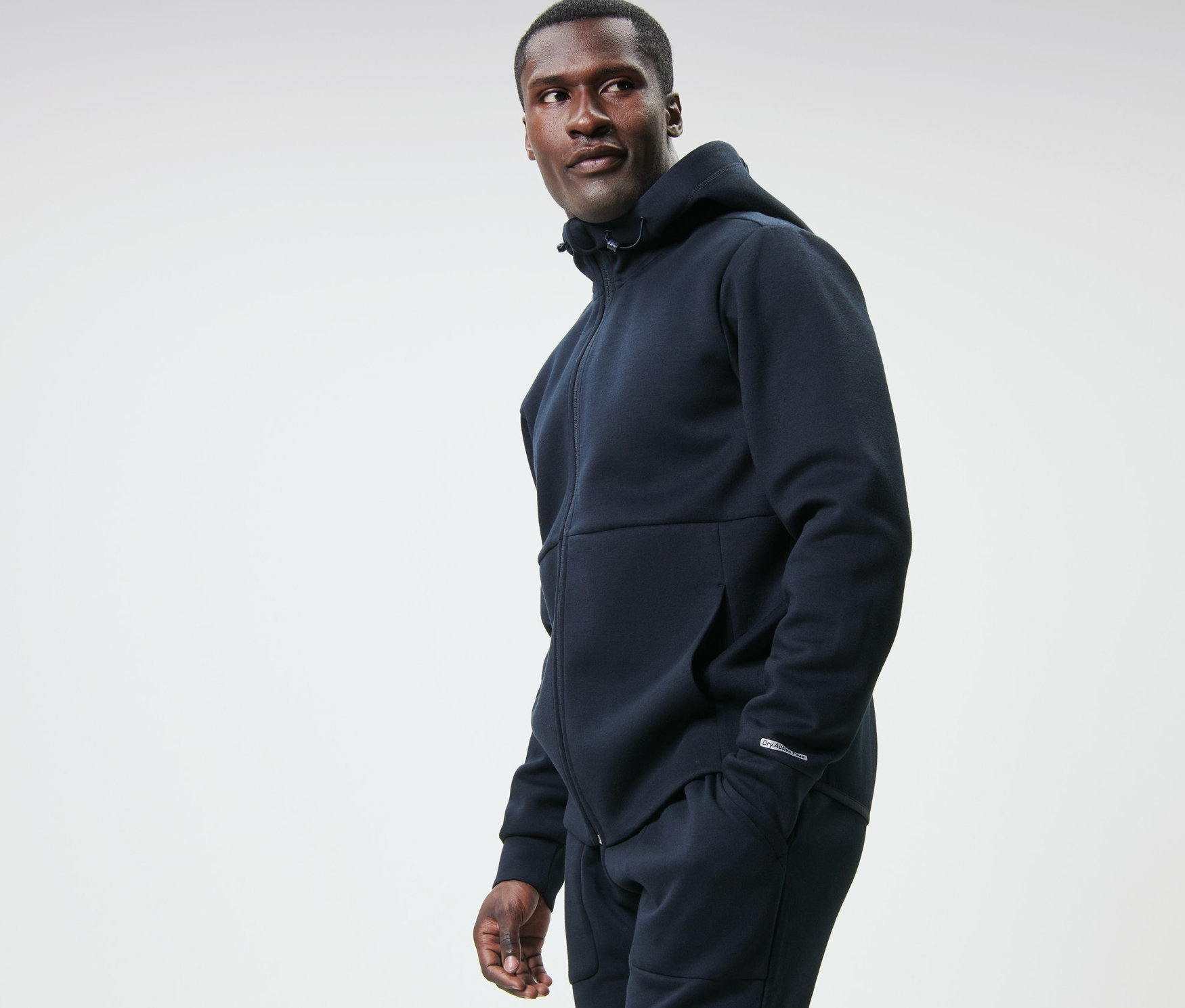 Muž v tmavomodrej funkčnej teplákovej mikine sa pozerá doľava.