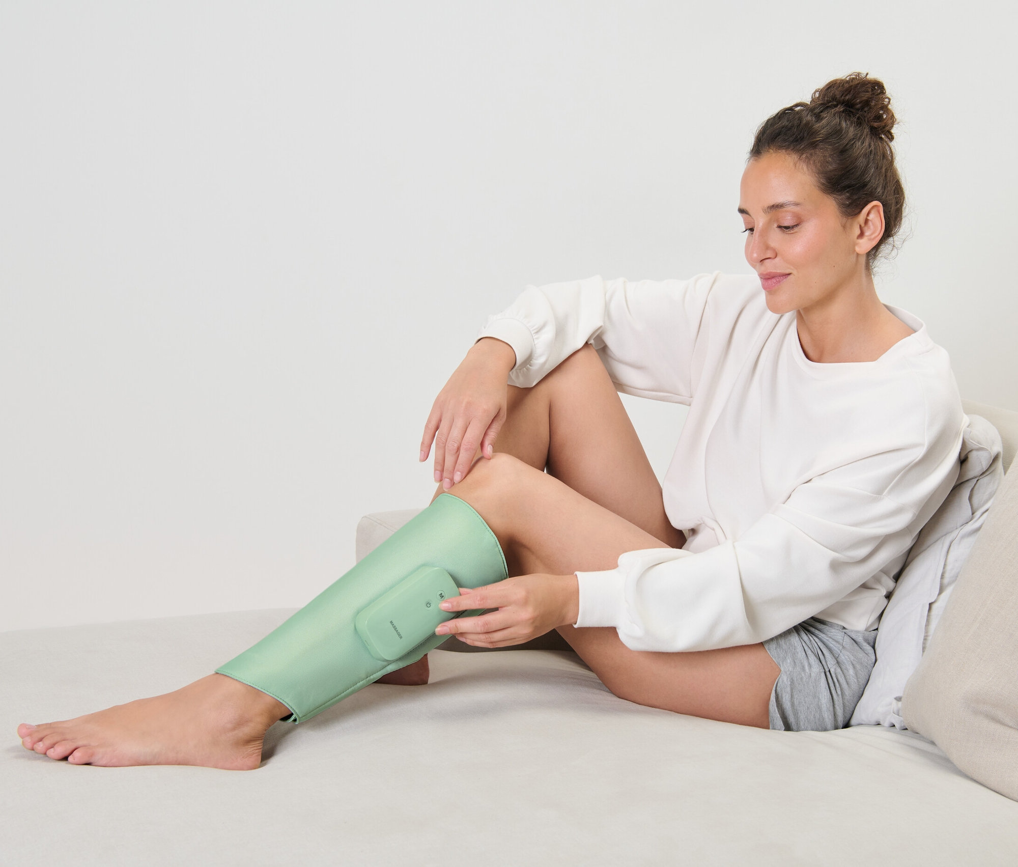 Žena sedí na gauči a používa akumulátorovú masážnu manžetu na nohu.