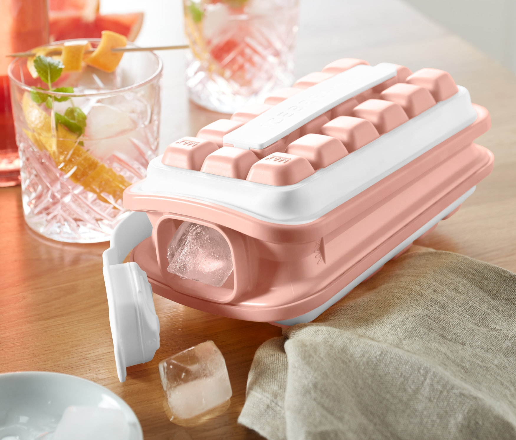 Ružová forma na ľad »ICEBREAKER® POP« na drevenom stole vedľa pohárov s nápojmi.