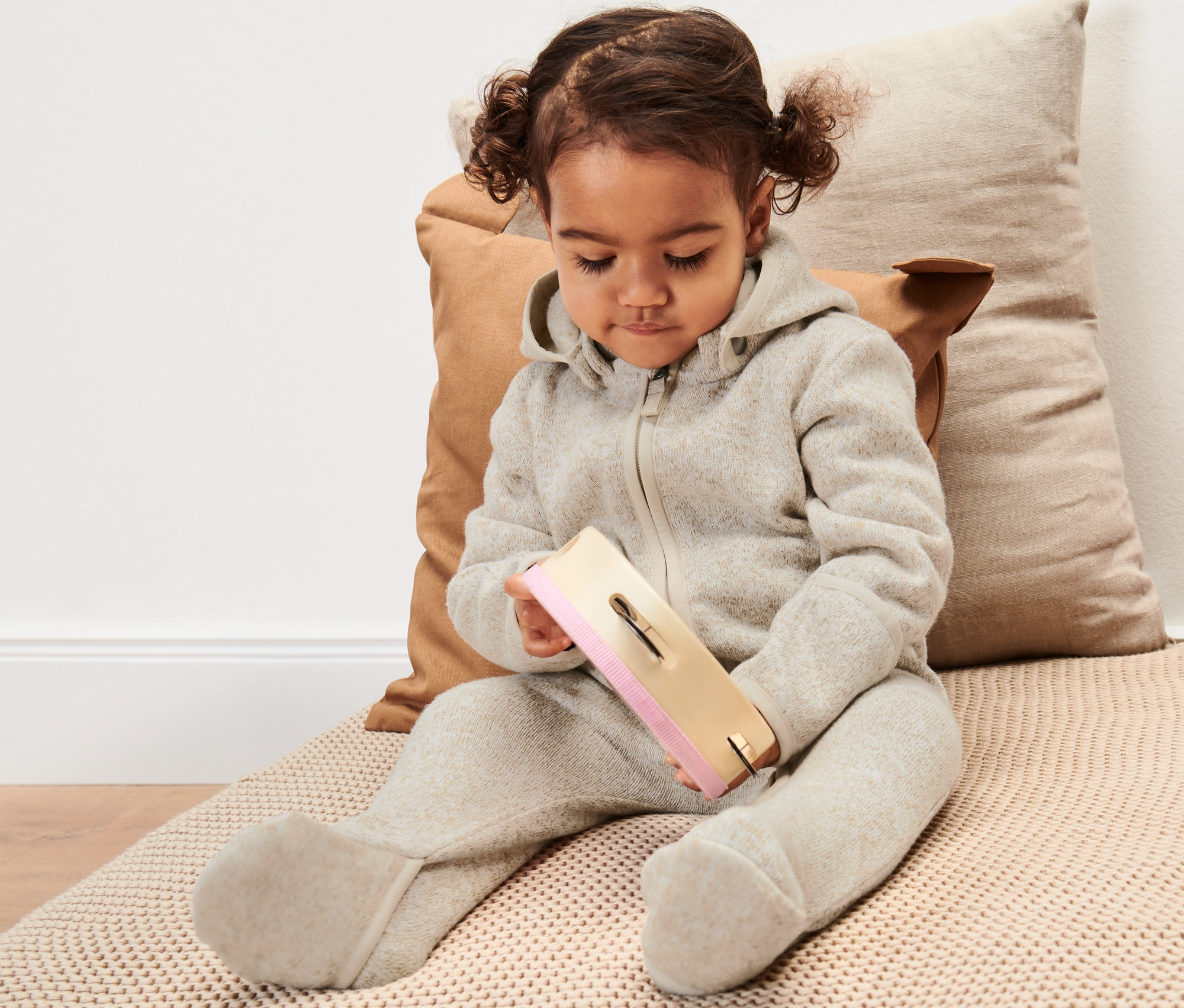 Batoľa sedí a hrá sa s hračkou, má na sebe detský overal z pleteného flísu.