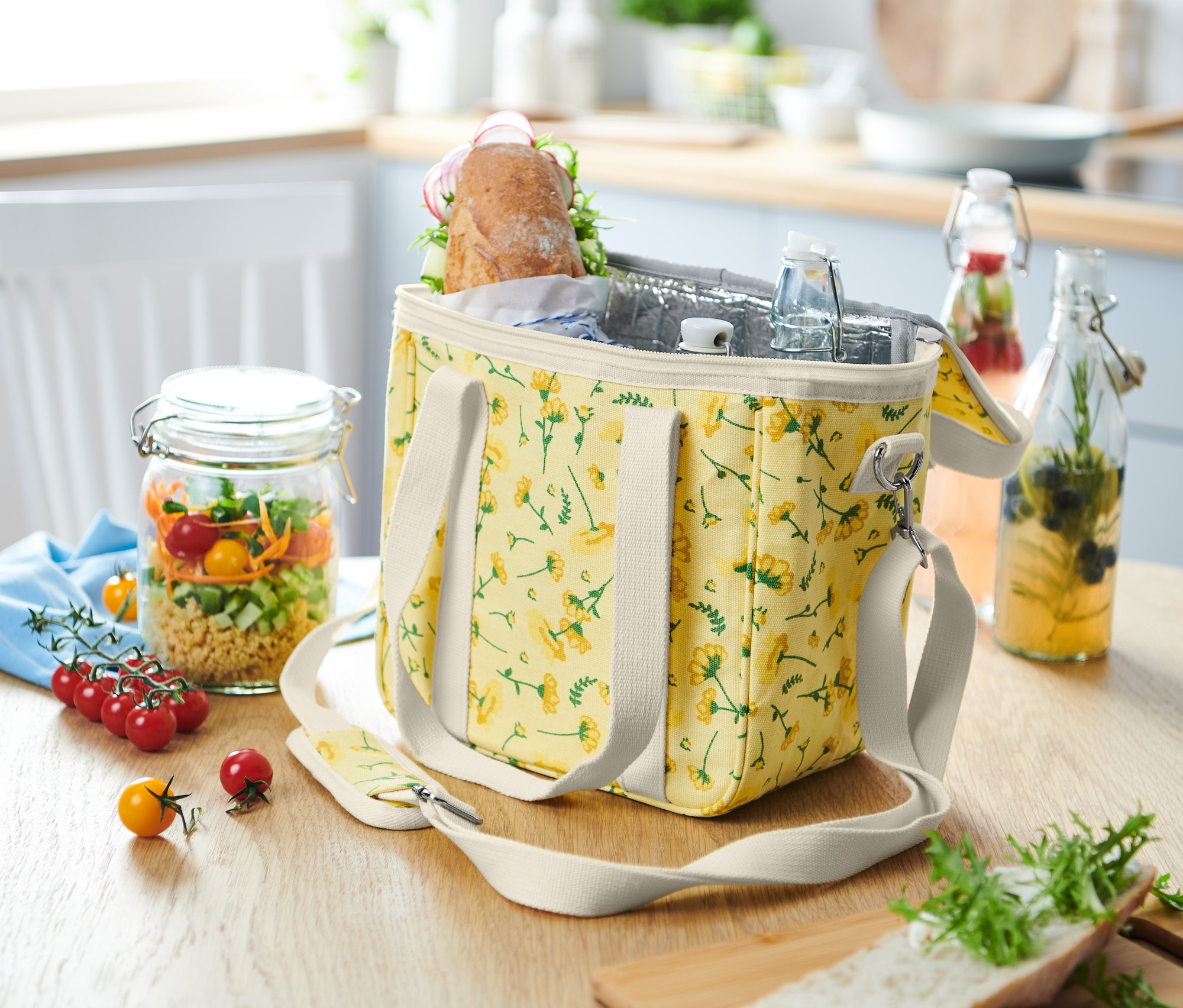 Chladiaca taška s kvetinovým vzorom stojí na stole vedľa pohára so šalátom.