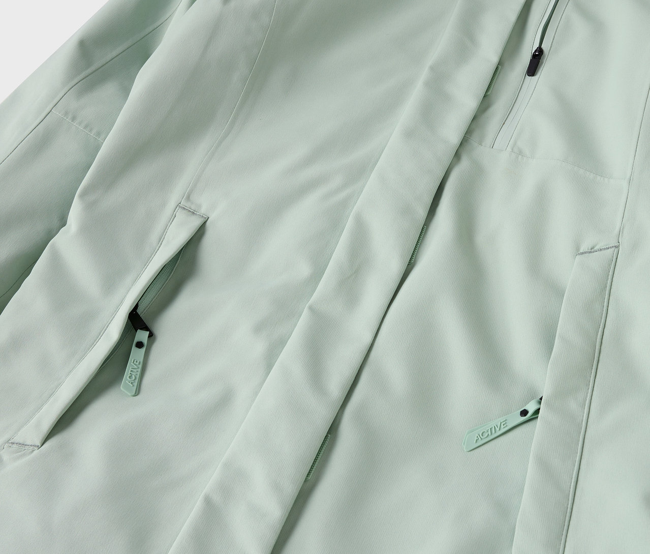 Detail svetlozelenej bundy s vreckami na zips.