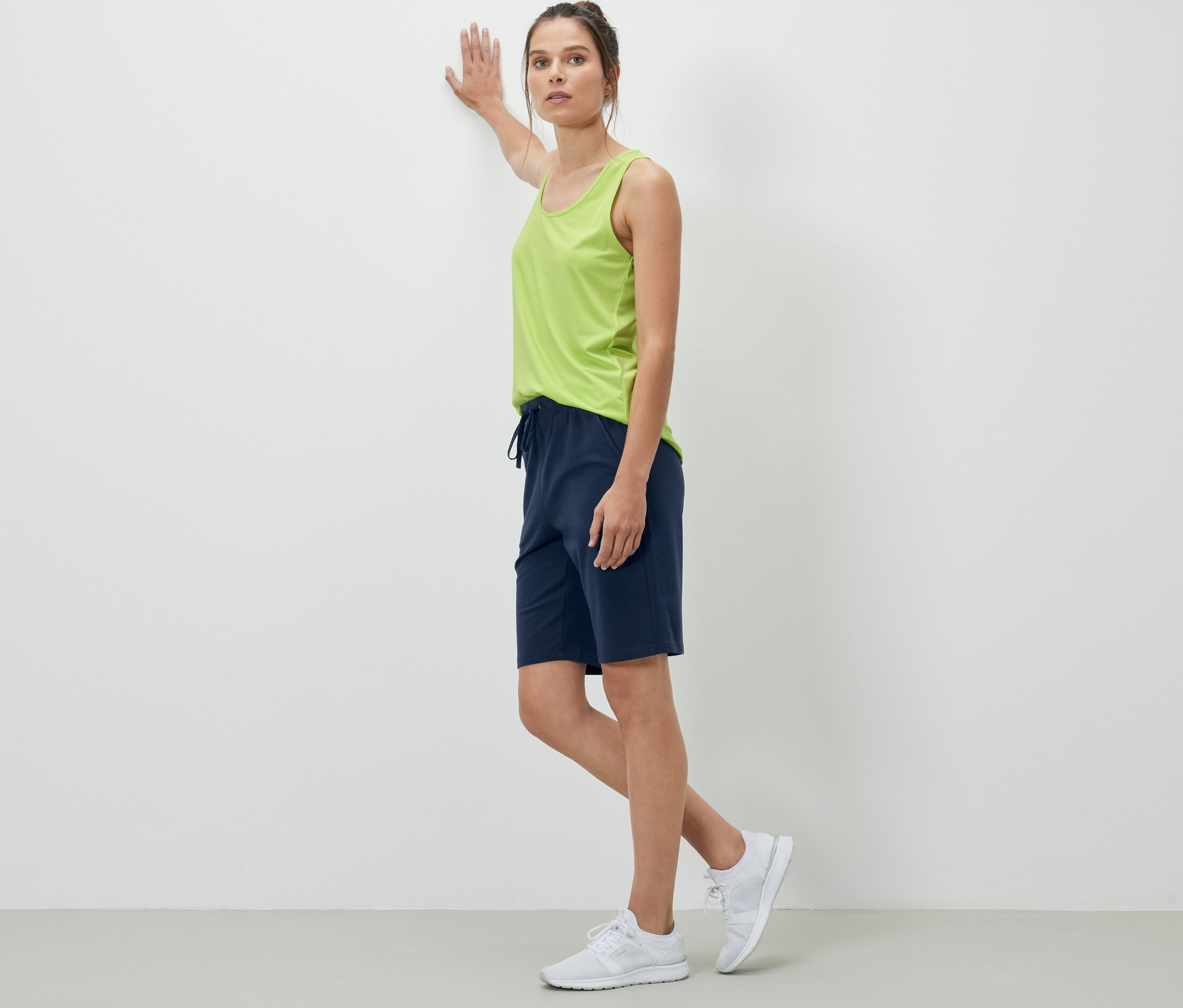 Žena opierajúca sa o stenu má na sebe tmavomodré teplákové šortky.