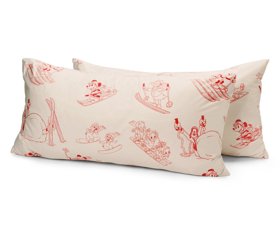 Dva biele vankúše s červenými kreslenými postavičkami lyžujúcich myšiek.