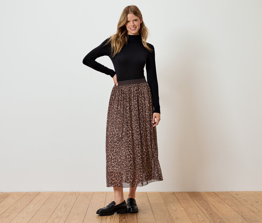 Žena stojí a pózuje v čiernej rolákovej blúzke a hnedej leopardej sukni.