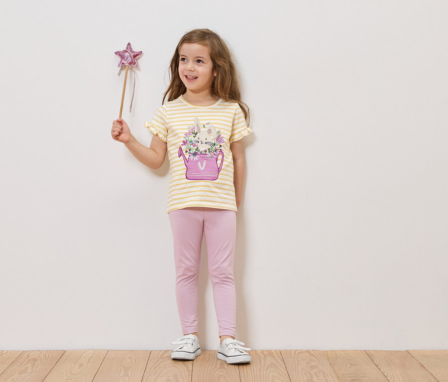 Dievča drží prútik s hviezdou, má na sebe tričko s obrázkom kanvy s kvetmi a ružové legíny.