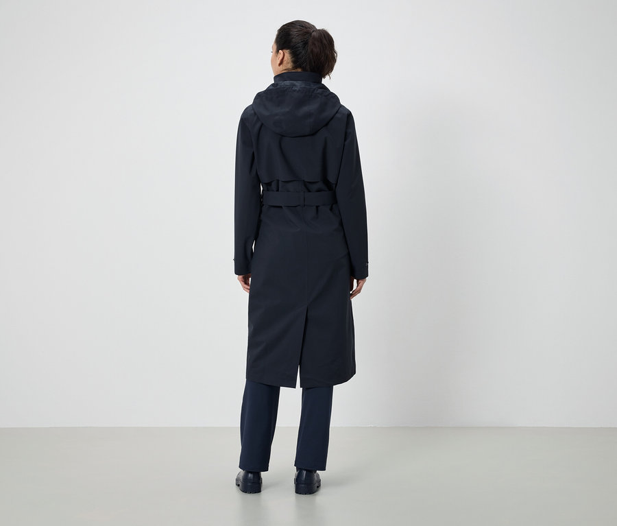 Zozadu je vidieť žena s konským chvostom, ktorá má na sebe tmavomodrý kabát s kapucňou a opasok a tmavomodré nohavice.