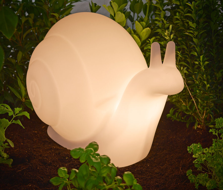 Snímka prémiového solárneho svietidla »Schnecke« umiestneného na zemi medzi rastlinami.