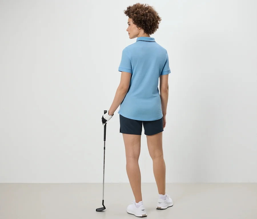 Žena zozadu drží golfovú palicu a má na sebe svetlomodré funkčné polo tričko.