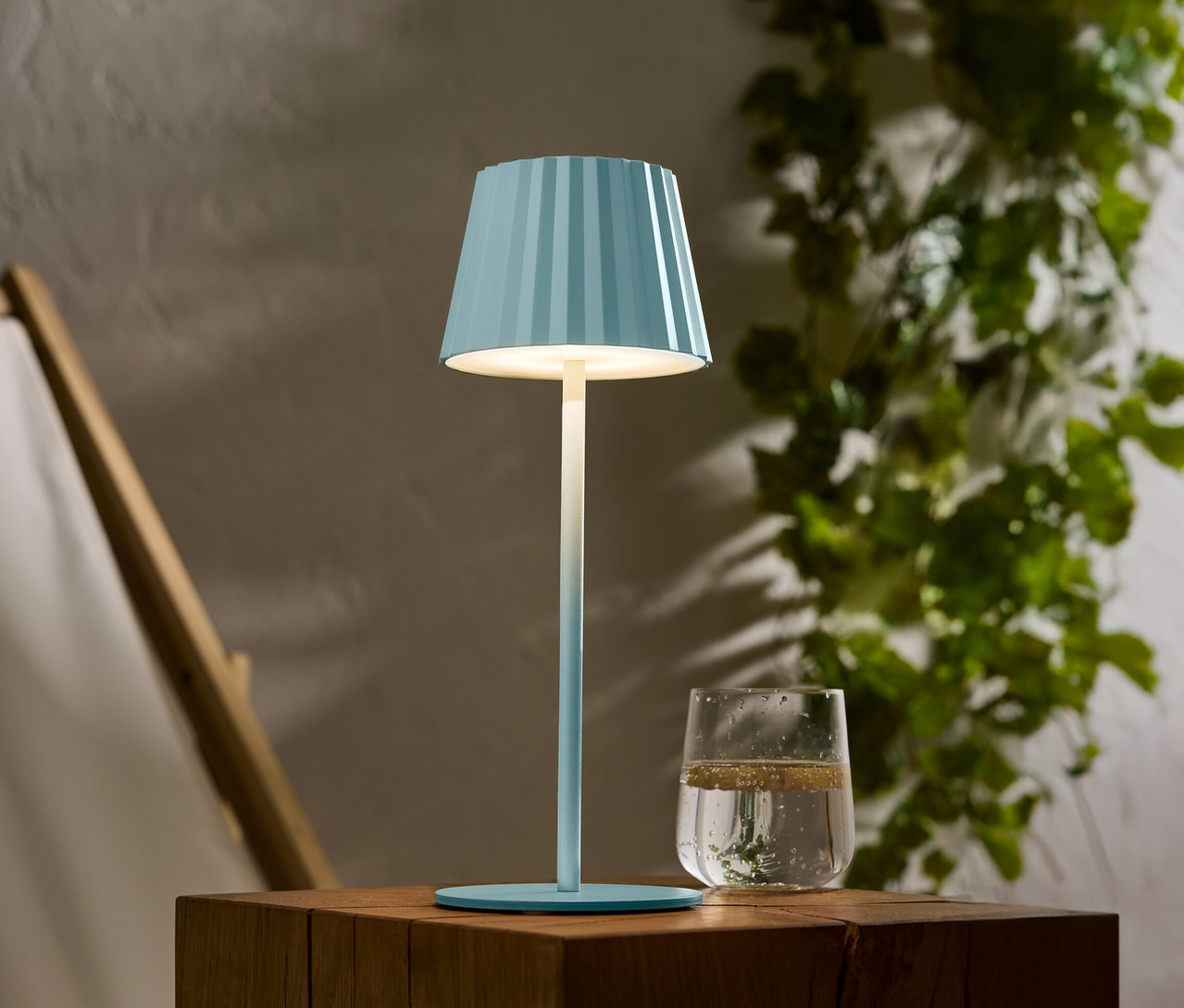 Modrá pruhovaná lampa stojí na drevenom stole vedľa pohára vody.