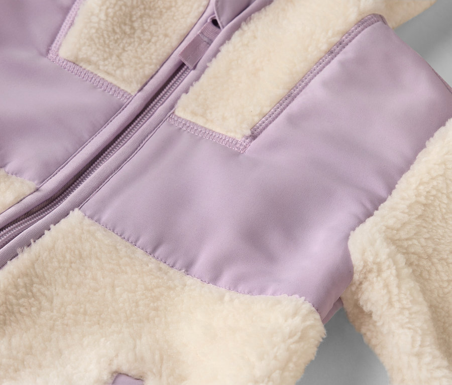 Detail bundy so zipsom a nadýchanými, krémovými a levanduľovými látkovými panelmi.
