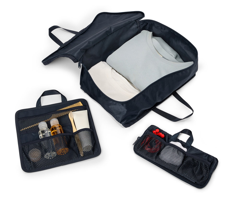 Tri otvorené, tmavomodré cestovné tašky s rúčkami a zipsami sú usporiadané na bielom pozadí. Tašky obsahujú oblečenie, kozmetiku a doplnky.