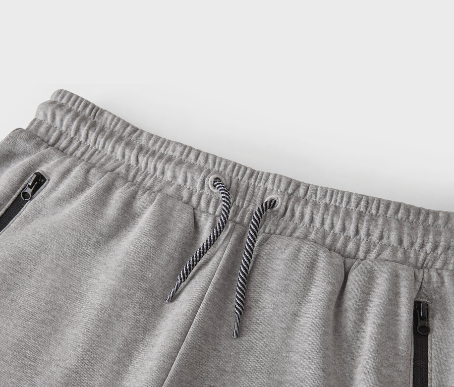 Detailný záber na pás sivých teplákov so šnúrkou a vreckami na zips.