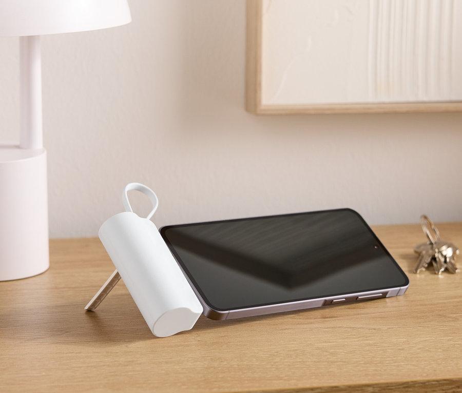 Na drevenom stole stojí lampa, tablet, zväzok kľúčov a biely valcovitý predmet s rúčkou.