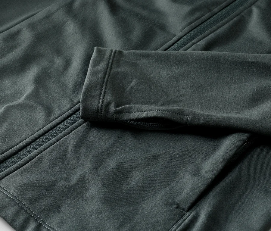 Detail tmavosivej bundy so zipsom a otvormi na palce na rukáve.