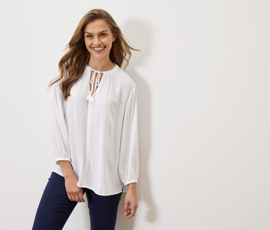 Žena má na sebe bielu blúzku s dlhými rukávmi a tmavomodré nohavice.