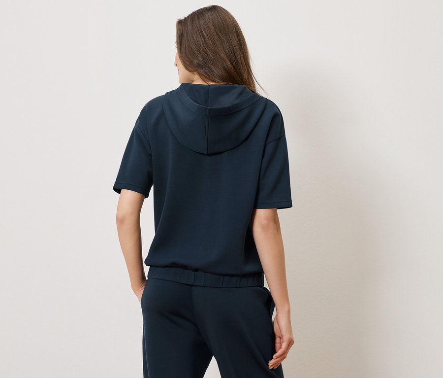 Pohľad zozadu na ženu v tmavomodrej mikine s kapucňou s krátkym rukávom a zodpovedajúcimi nohavicami.