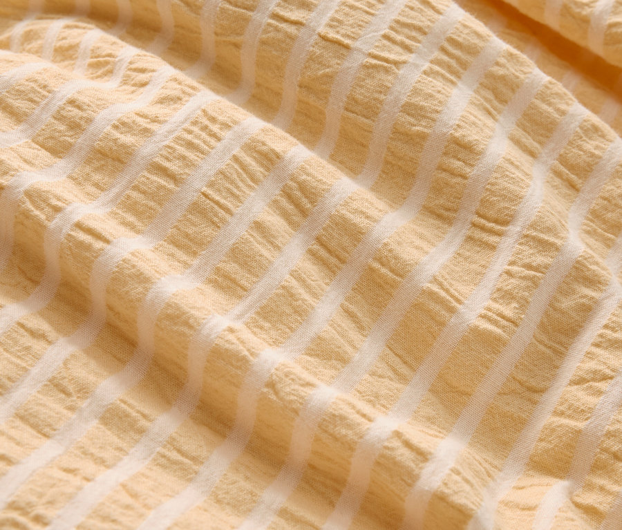 Detail záberu pokrčenej, svetložltej látky s bielymi pruhmi.