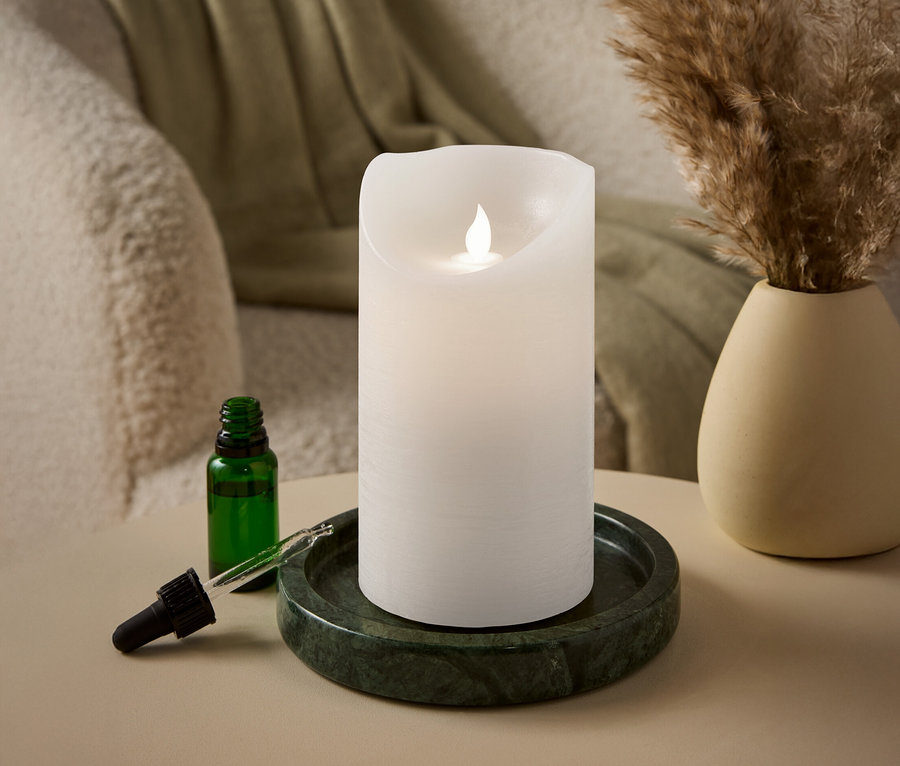 Biela valcová sviečka s LED plameňom stojí na zelenom mramorovom podnose vedľa zelenej sklenenej fľaše s pipetou.