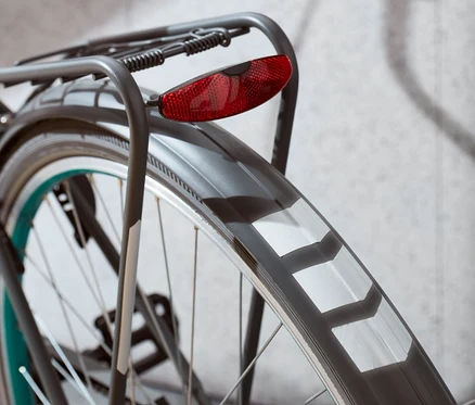 Detail zadného kolesa bicykla s červeným svetlom a reflexnými nálepkami.