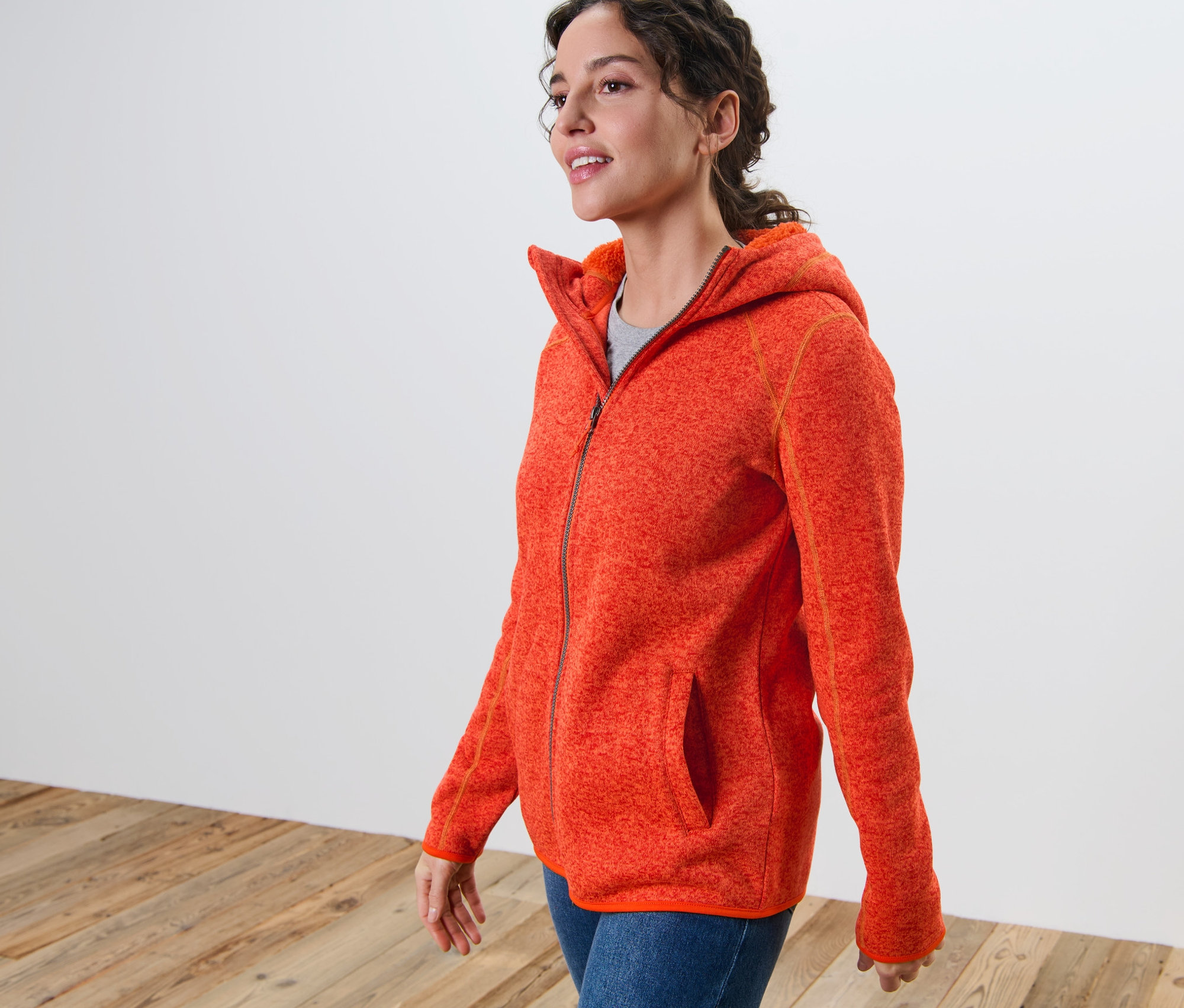 Žena má na sebe oranžovú melírovanú bundu z pleteného flísu s kapucňou.