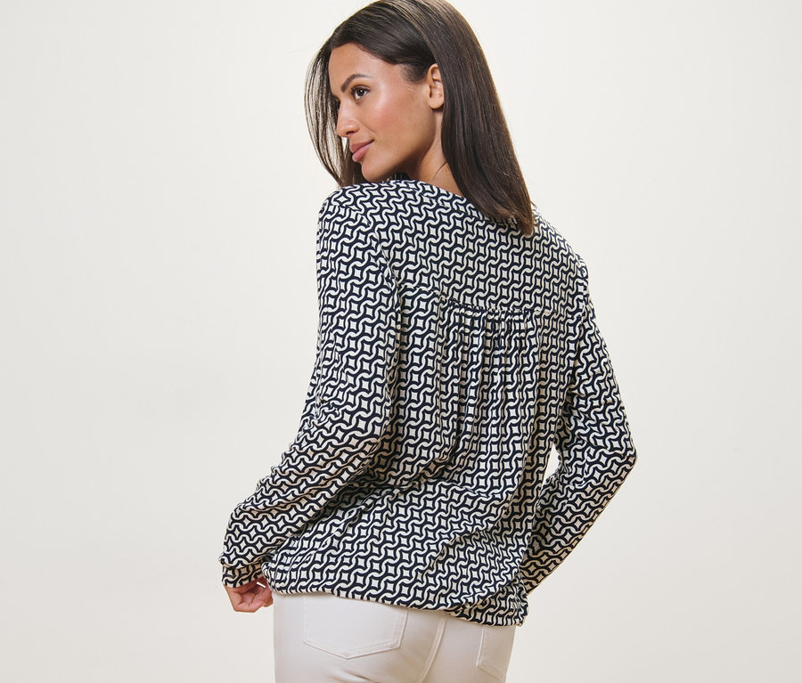 Žena sa pozerá cez rameno a má na sebe blúzkové tričko s potlačou, námornícke modré.