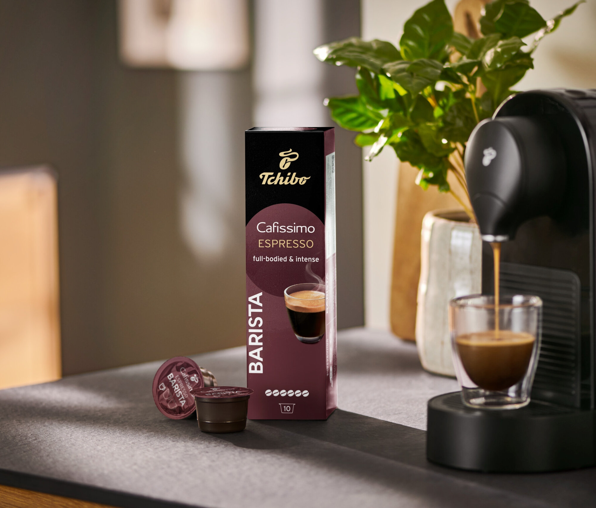 Espresso tečie do sklenice z kávovaru Cafissimo BARISTA vedľa balenia 10 kapsúl.