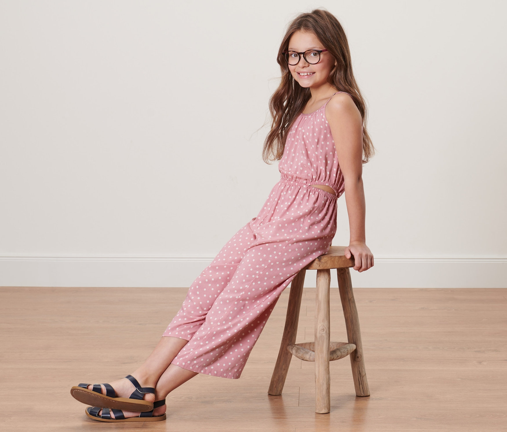 Dievča sedí na stoličke a má na sebe detský tkaný overal v 7/8 dĺžke.