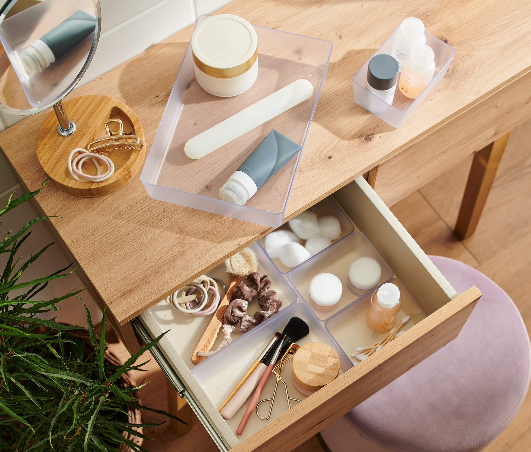 Otvorená zásuvka dreveného toaletného stolíka obsahuje súpravu organizérov do zásuviek s kozmetikou.