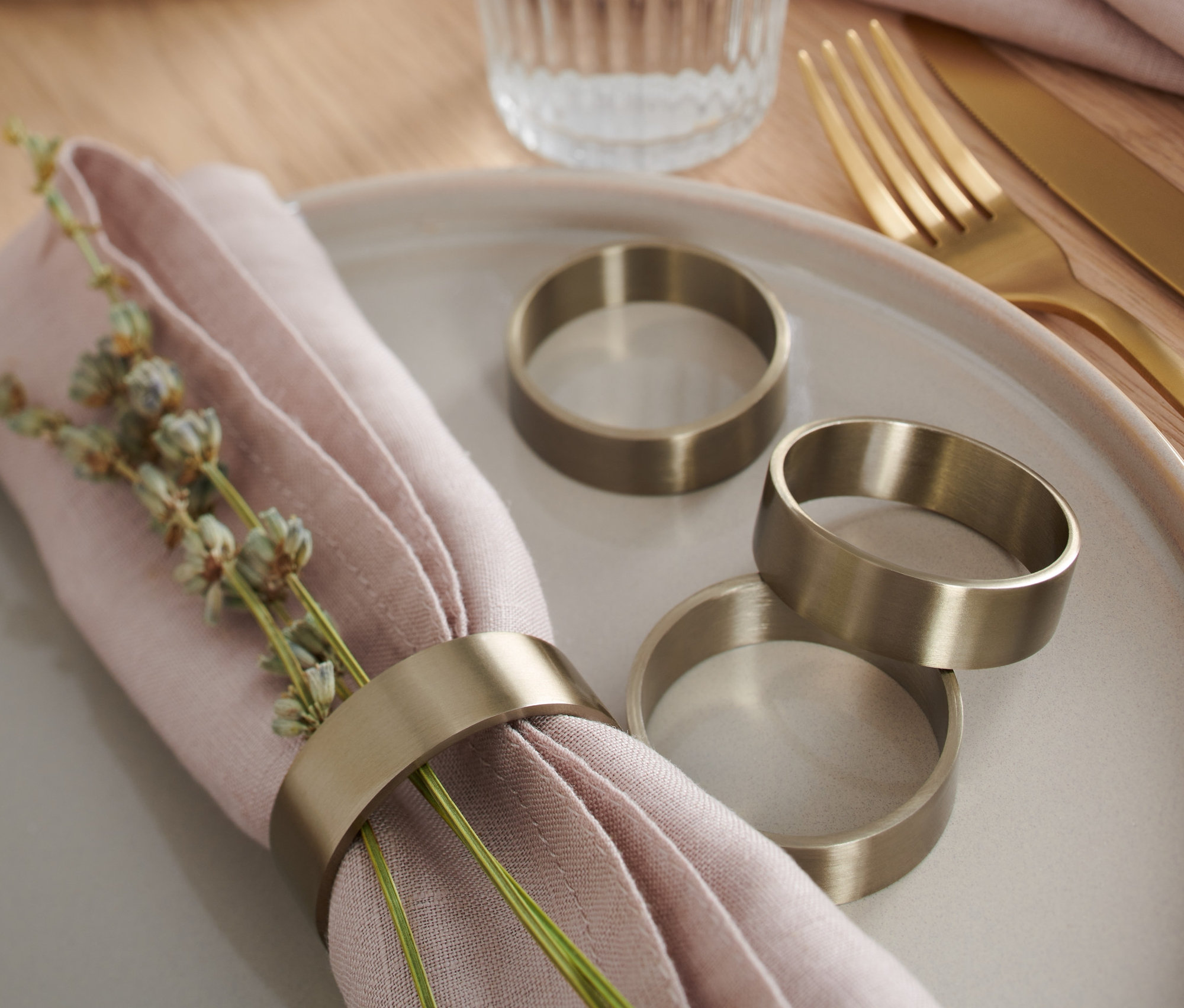 Na tanieri leží ružový obrúsok s dekoráciou a krúžkom na obrúsky, 4 ks. Vedľa neho sú tri krúžky na obrúsky.