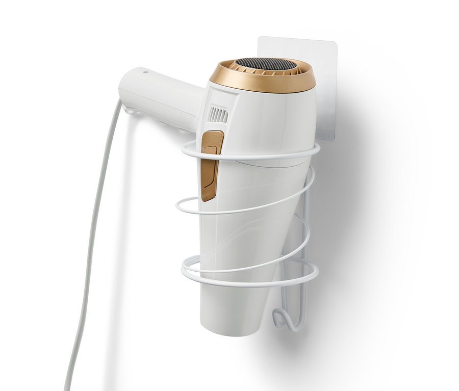 Biely držiak na sušič vlasov je pripevnený na bielej stene a drží biely sušič vlasov.