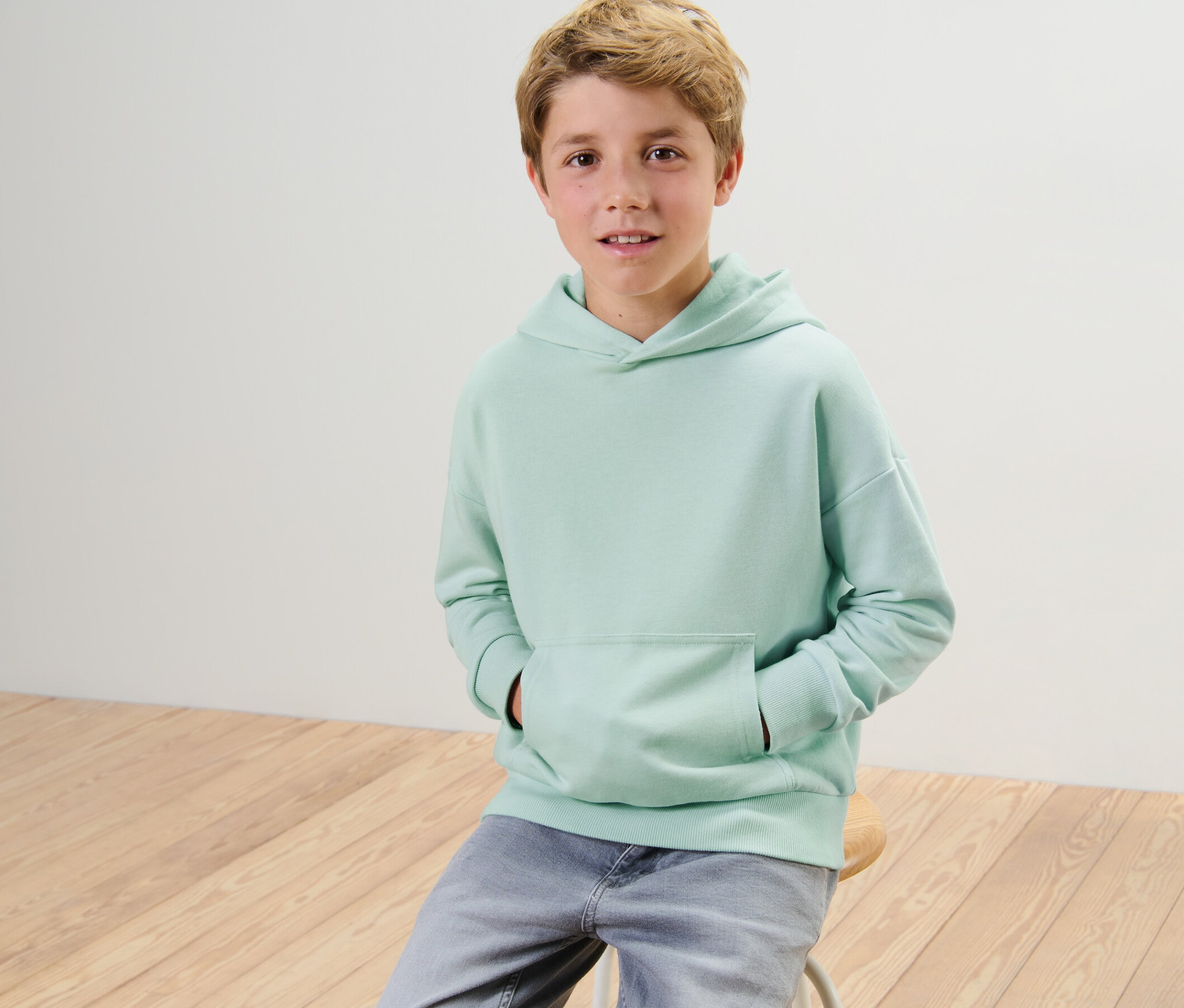 Chlapec sedí na stoličke a má na sebe detskú mikinu z teplákoviny.