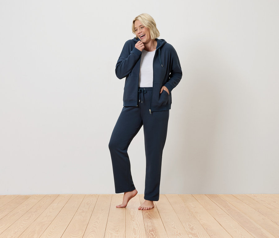 Žena stojí a usmieva sa, má na sebe modrú teplákovú súpravu.