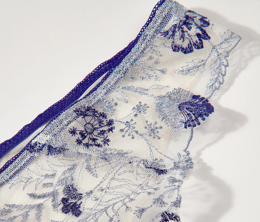 Detail bielych tangáčov Passionata »Chloe« s modrou kvetinovou výšivkou.