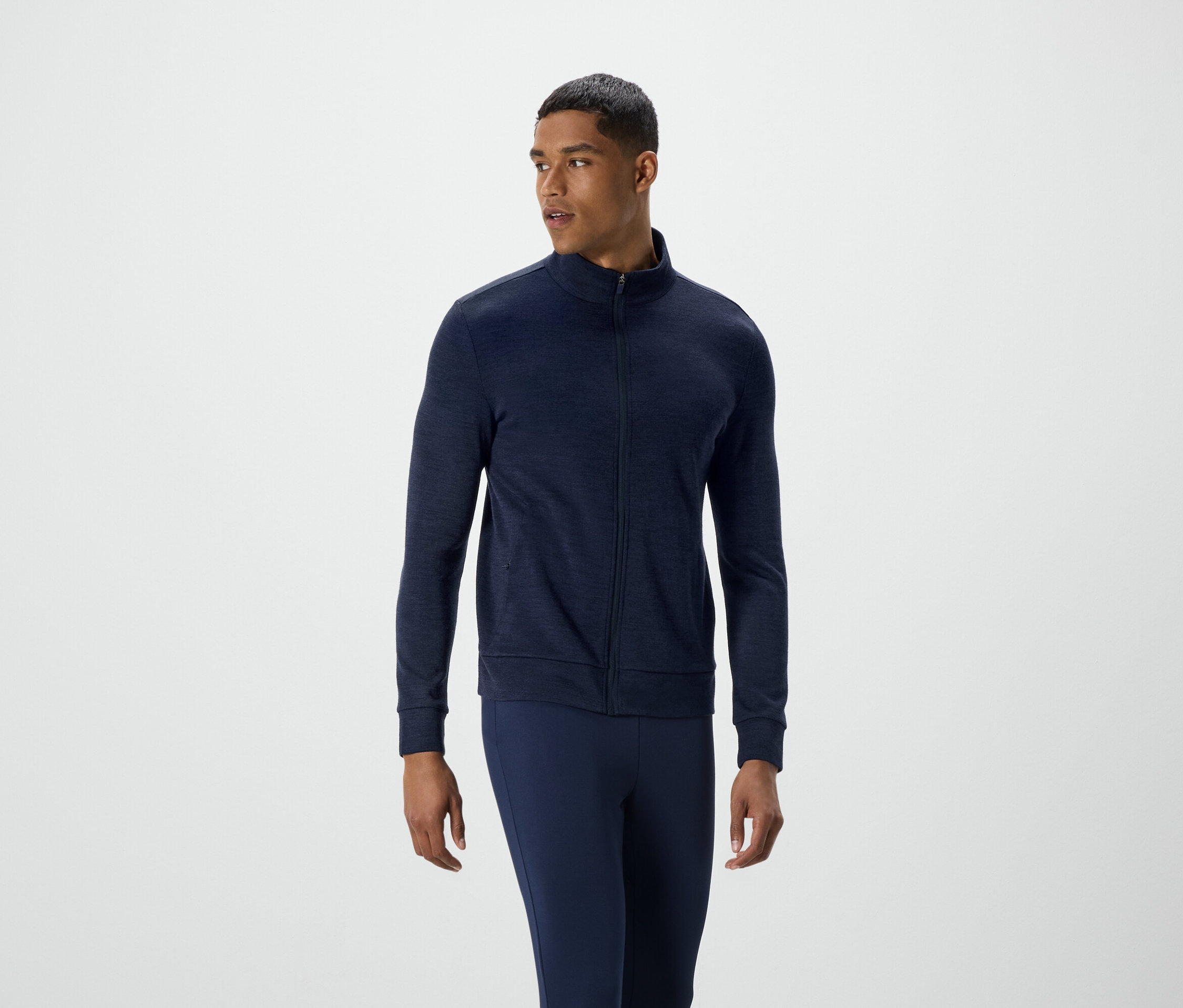 Muž v tmavomodrej bunde na zips a nohaviciach sa pozerá doľava.