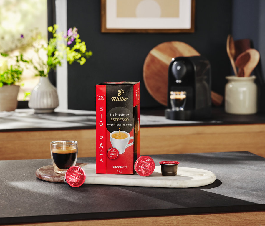 Na stole stojí balenie kapsúl Cafissimo Espresso, sklenica s espressom a kávovar.