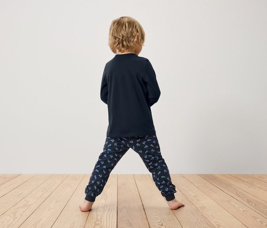 Chlapec chrbtom, má na sebe tmavomodré pyžamo s dlhým rukávom a vzorované nohavice.