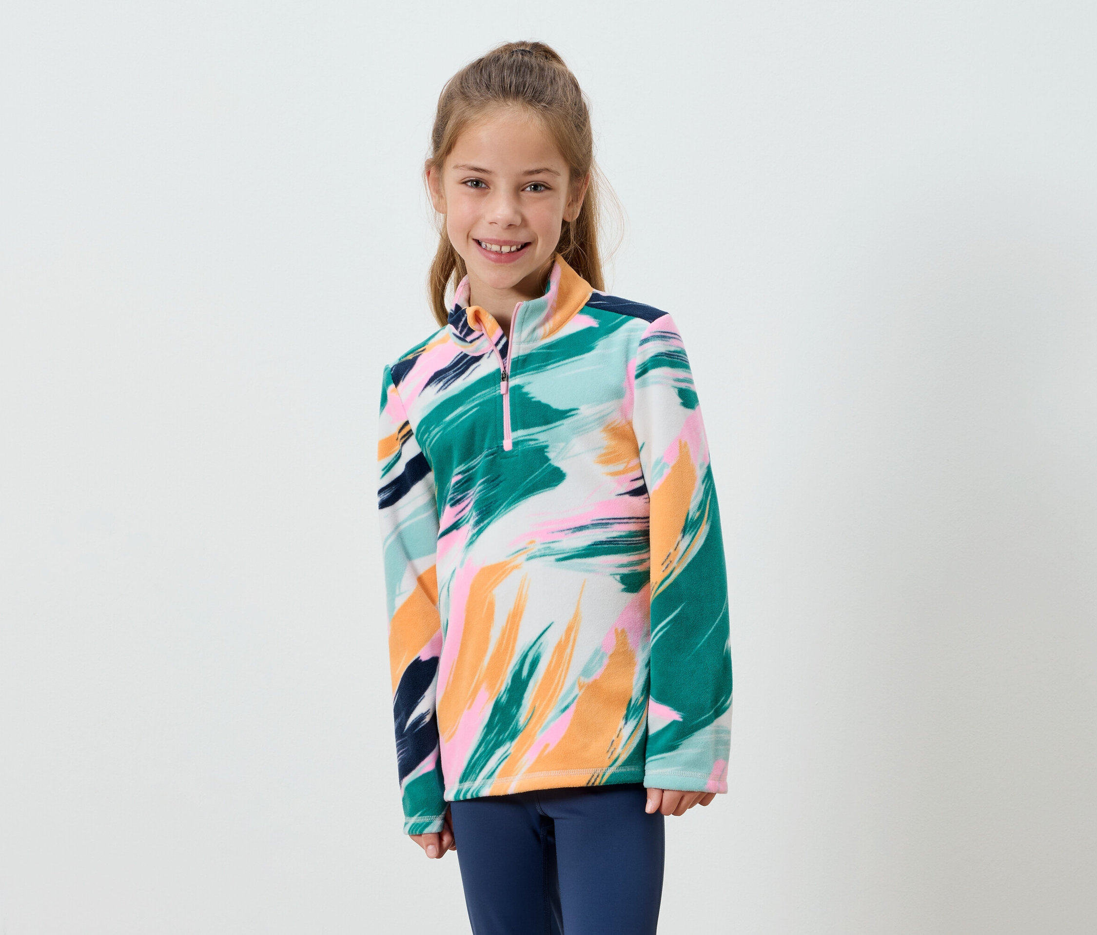 Usmievajúce sa dievča má na sebe fleece s abstraktnou potlačou a modré nohavice.