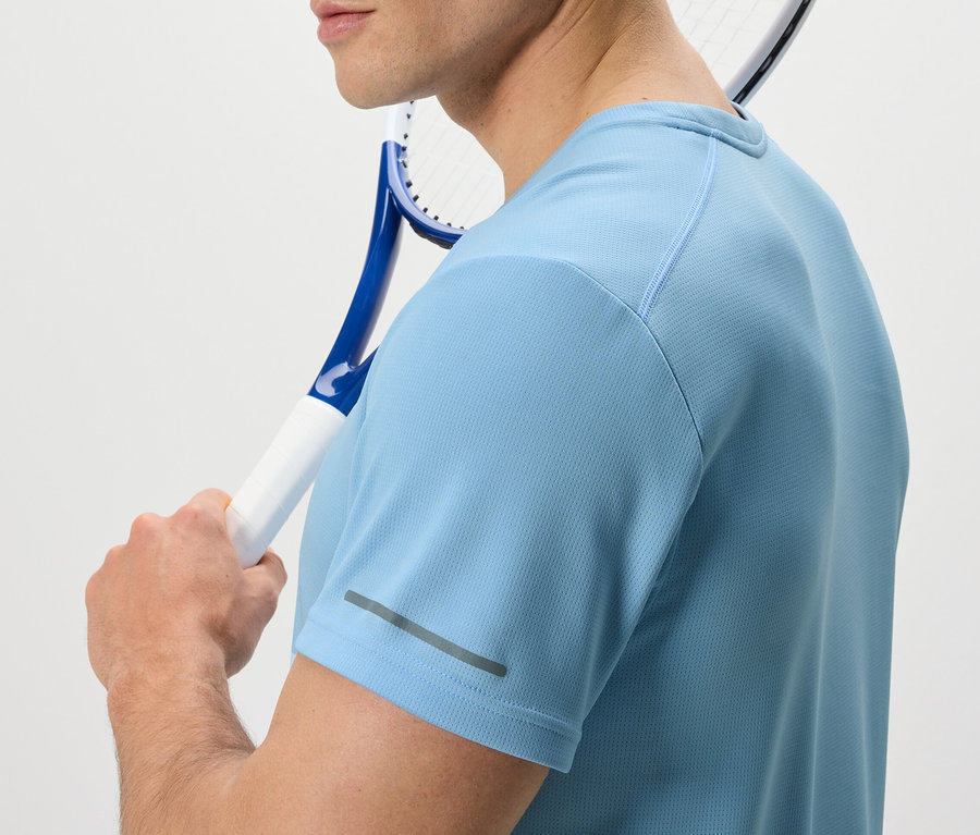 Muž s tenisovou raketou cez rameno má na sebe svetlomodré funkčné tričko.