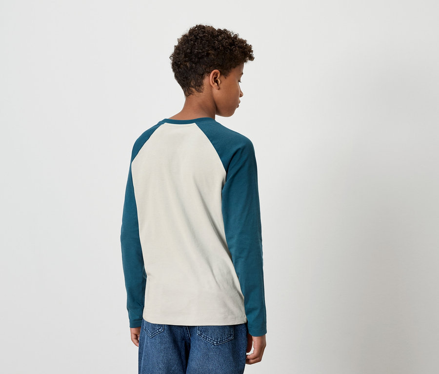 Mladý muž chrbtom k fotoaparátu má na sebe dvojfarebné tričko s dlhým rukávom a džínsové nohavice.