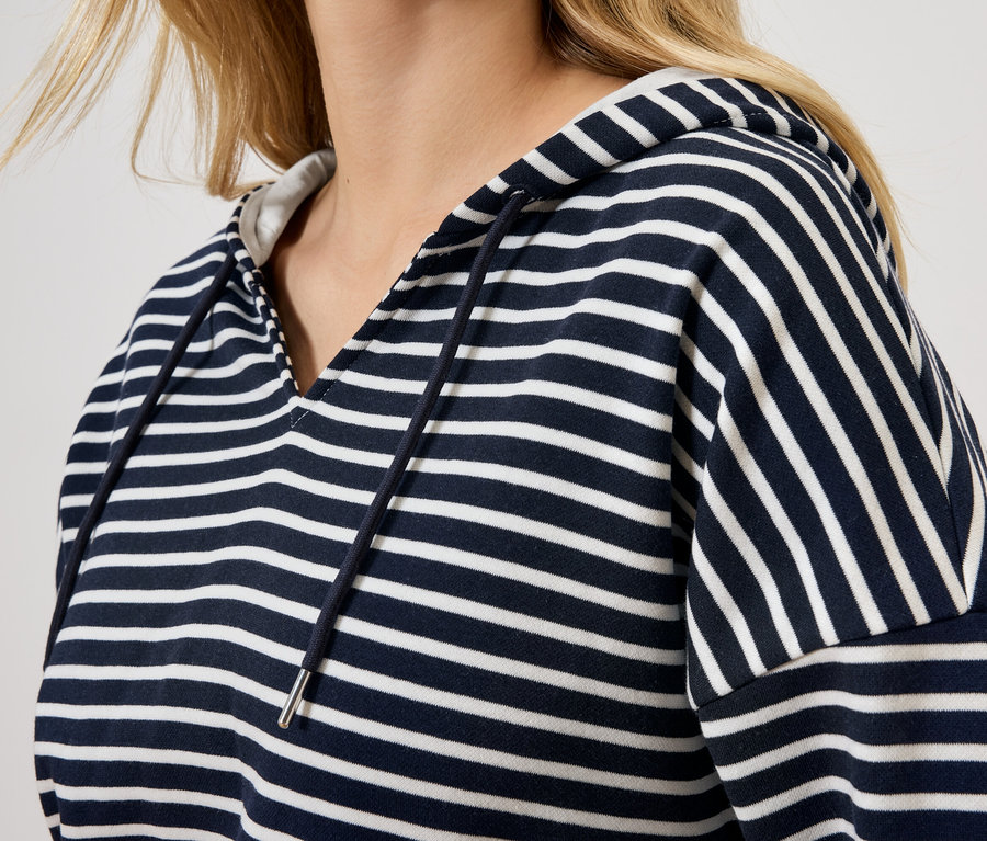 Blondínka má na sebe pruhovanú mikinu s kapucňou.