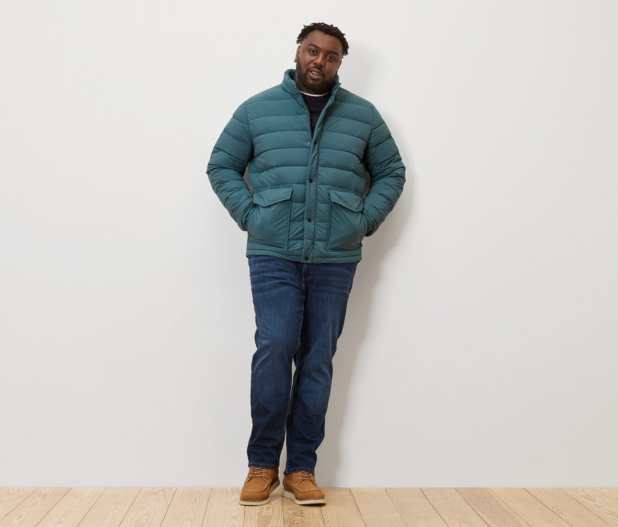 Muž stojí a má na sebe prešívanú bundu, džínsy a topánky.