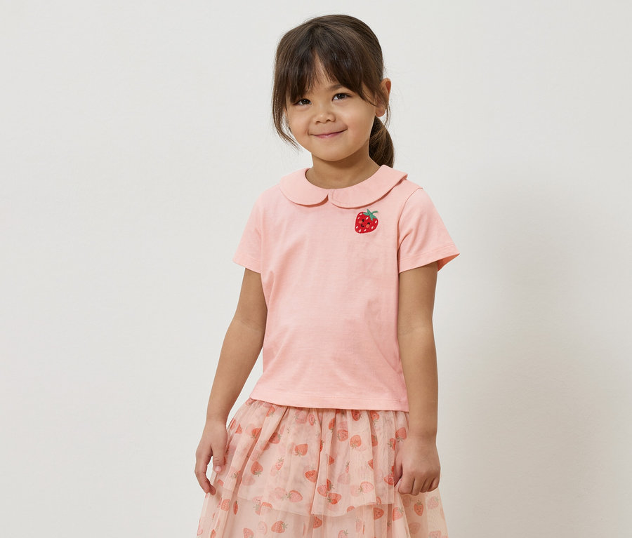 Dievča v ružovom tričku s aplikáciou jahody a ružovej sukni s jahodovým vzorom.