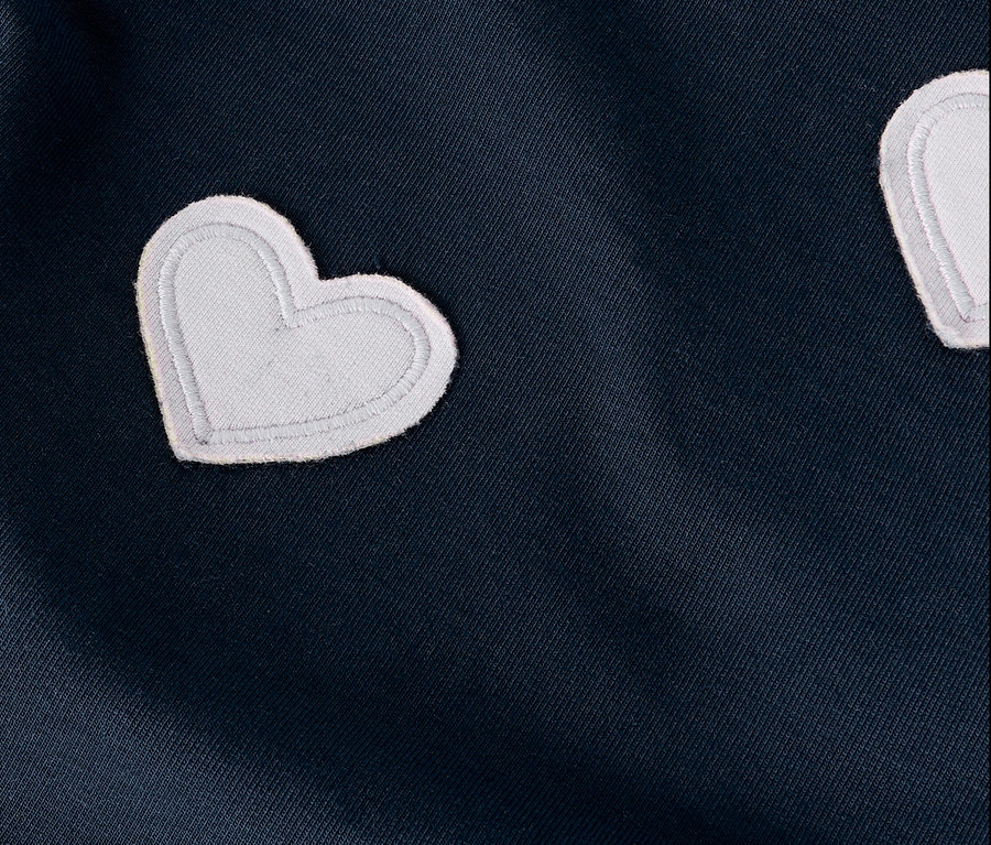 Detail tmavomodrej látky s bielymi aplikáciami v tvare srdca.