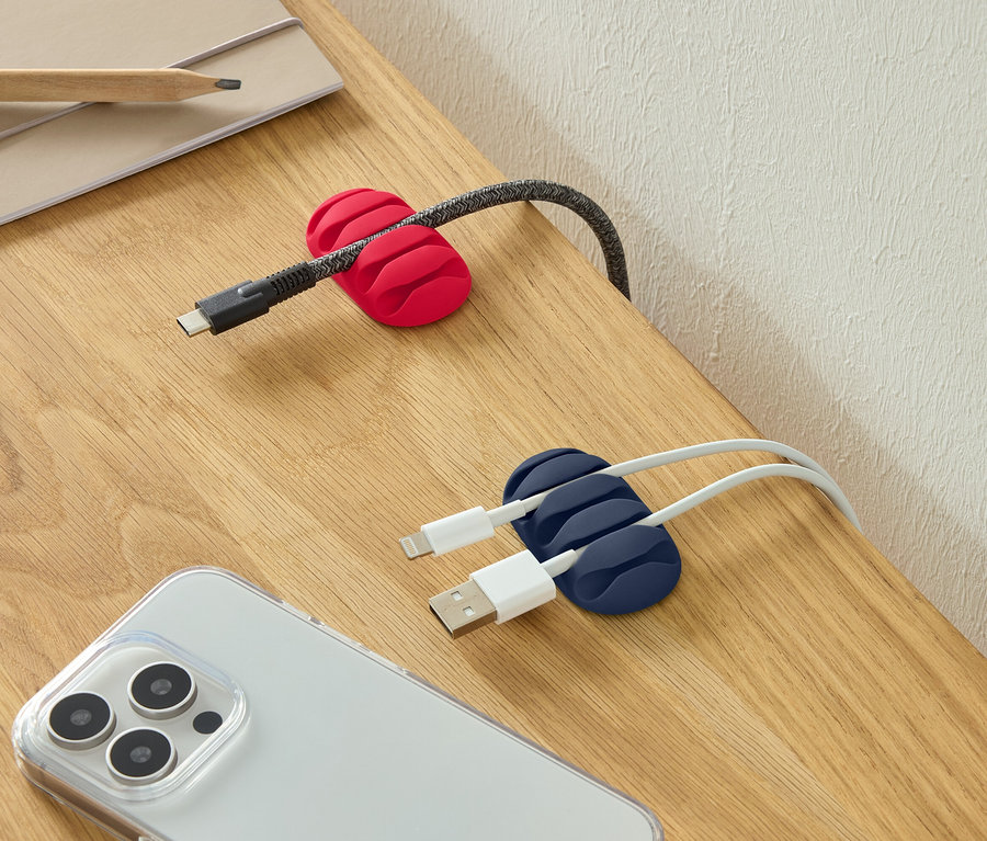 USB-C kábel v červenom držiaku na káble, dva USB káble v modrom držiaku na káble a smartfón na stole.