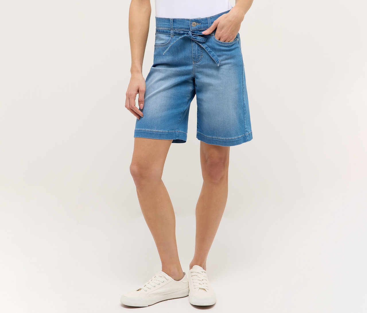 Žena v svetlomodrých šortkách Angels Denim »Lia City« a bielych topánkach, ruka vo vrecku.