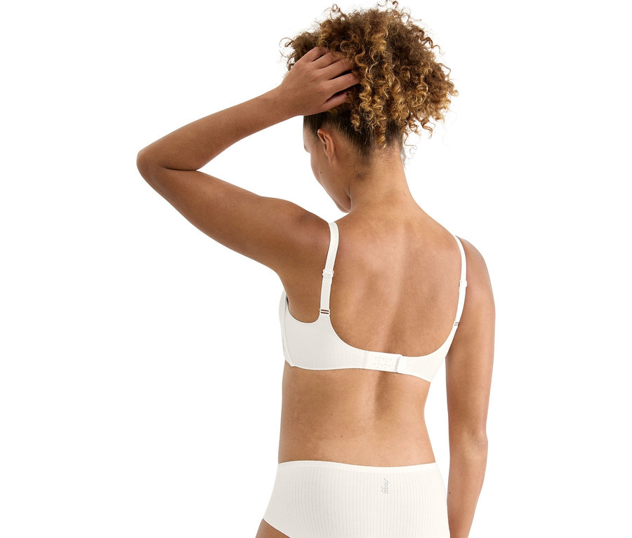 Pohľad zozadu na ženu s kučeravými vlasmi, ktorá má na sebe bielu podprsenku a nohavičky a drží si ruku vo vlasoch.