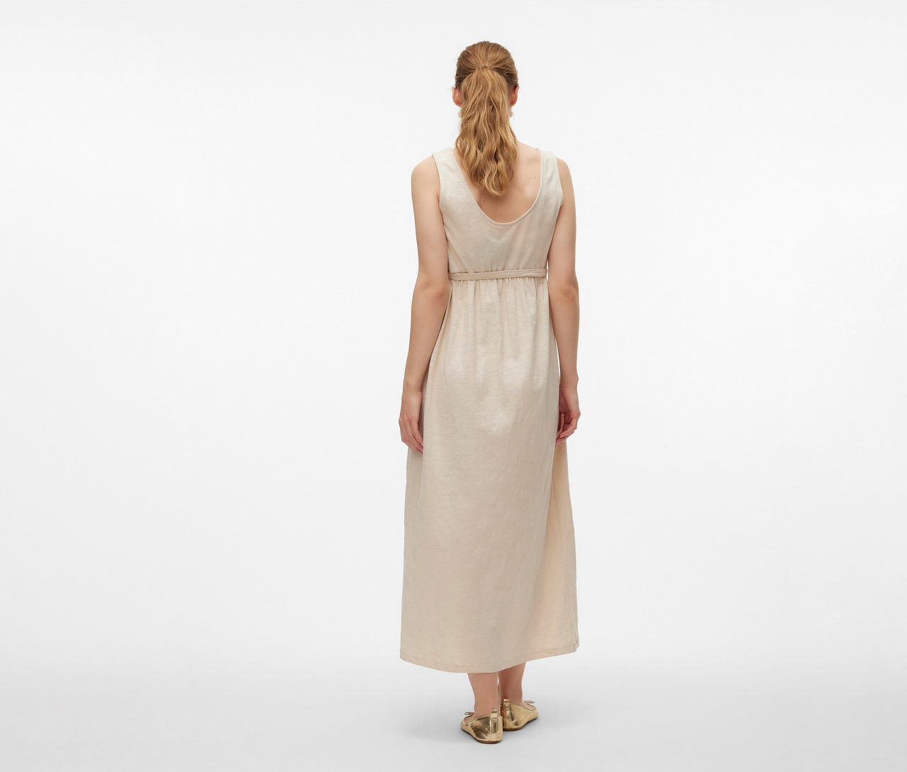 Pohľad zozadu na ženu v tehotenských šatách MAMALICIOUS »MLEVI LIA« a zlatých topánkach na bielom pozadí.