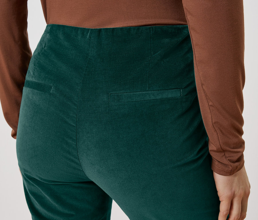 Detailný záber na zadnú časť osoby v zelených menčestrových nohaviciach a hnedom tope.